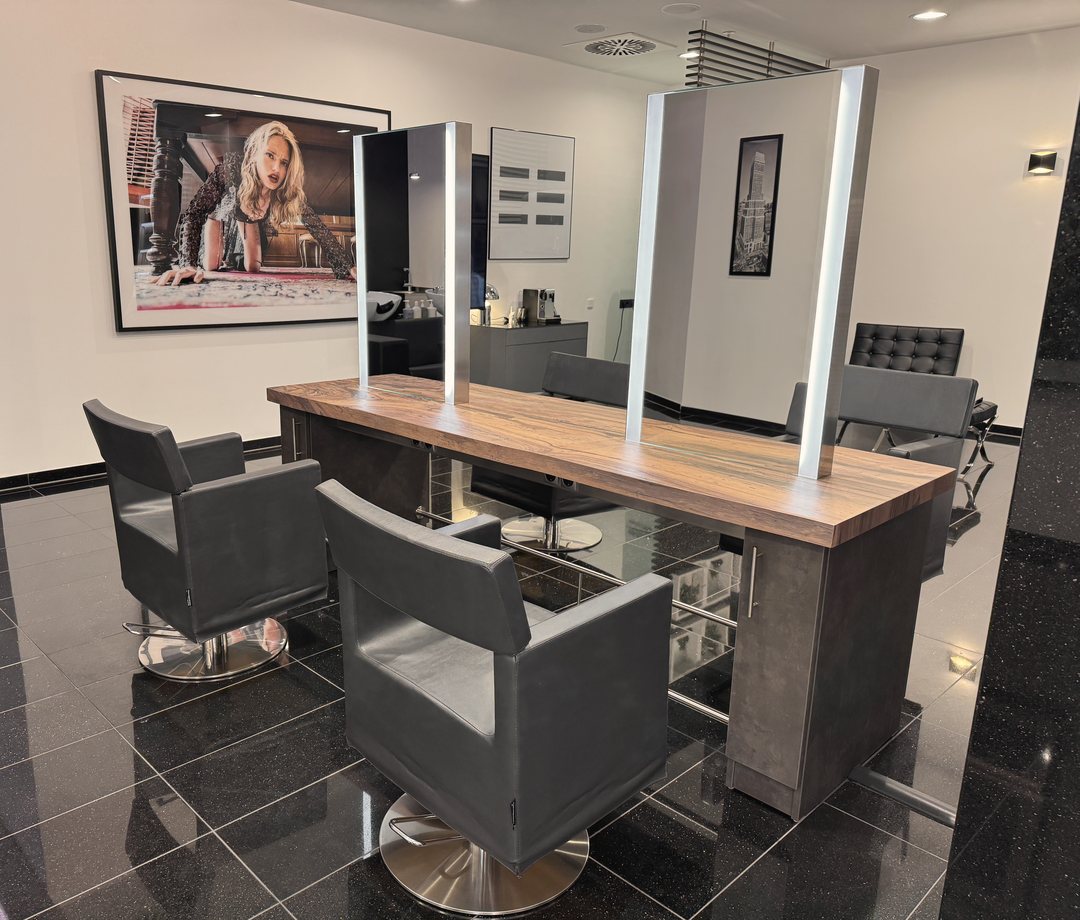 Arbeitsplatz mit Holztisch, hellen Spiegeln und grauen Friseurstühlen